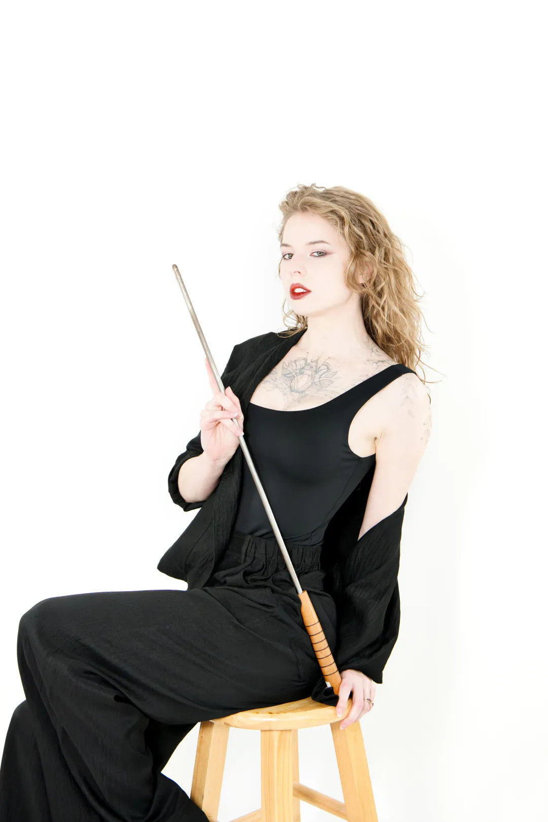 Brittany Elleway seated on a stool with a cane, in black, on a white backdrop